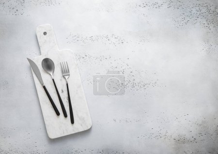Téléchargez les photos : Table de cuisine en marbre avec fourchette, couteau et cuillère sertis de poignées noires. Vue du dessus. - en image libre de droit