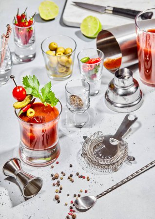 Foto de Copa de cóctel Bloody Mary con utensilios de bar, cal, pimientos, aceitunas en tablero de luz con luz solar.. - Imagen libre de derechos