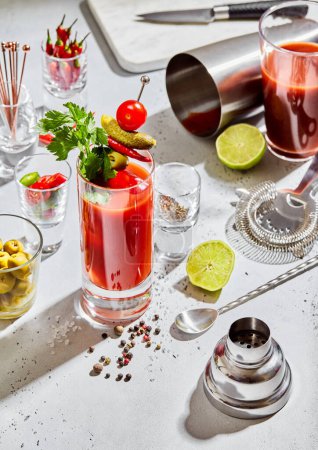 Foto de Mezcla de cócteles Bloody Mary con cuchara de bar, agitador y colador en el fondo ligero con lima, aceitunas y pimienta. - Imagen libre de derechos
