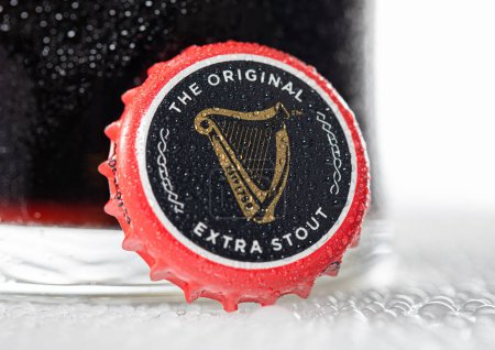 Photo for LONDON, UK - DECEMBER 22, 2022: Guinness stout draught original beer bottle cap with dew and cold glass on white. - Royalty Free Image