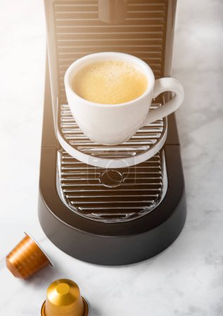 Foto de Taza de café blanco y cafetera espresso casera con cápsulas de café en cocina de mármol blanco - Imagen libre de derechos