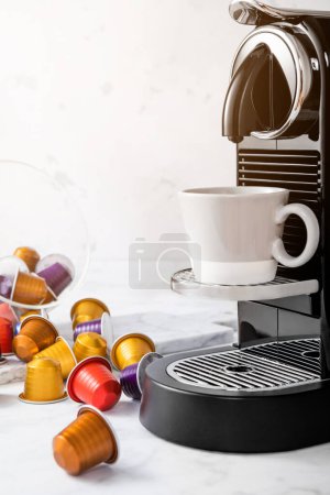 Foto de Cafetera con taza de café expreso y cápsulas de café vainas en luz mañana fondo de cocina y luz solar - Imagen libre de derechos