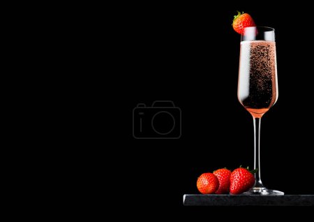 Téléchargez les photos : Élégant verre de champagne rose rose avec fraise sur le dessus sur un panneau de marbre noir sur fond noir. - en image libre de droit