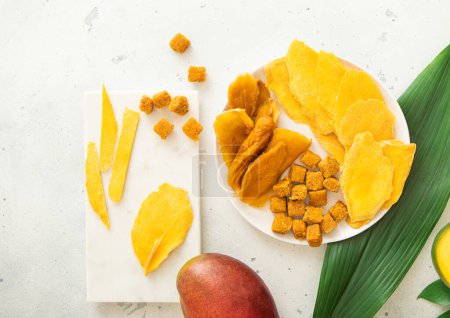 Téléchargez les photos : Morceaux et boules de mangue séchés dans des assiettes en marbre sur un panneau lumineux avec des fruits frais.. - en image libre de droit