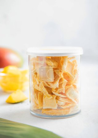 Téléchargez les photos : Congeler les mangues séchées pour les céréales dans un bocal en plastique sur fond clair. - en image libre de droit