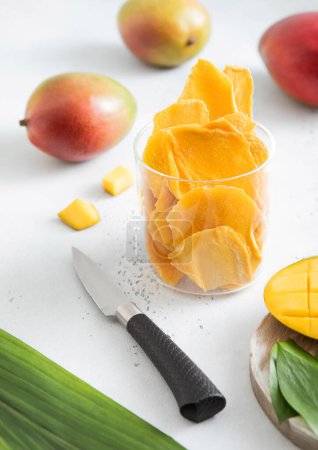 Téléchargez les photos : Mangue séchée dans un bocal en verre avec des fruits crus et un couteau sur un plateau léger.. - en image libre de droit