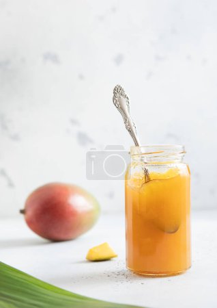 Téléchargez les photos : Pot en verre avec cuillère de purée de confiture de mangue biologique fraîche sur fond clair avec feuille. - en image libre de droit