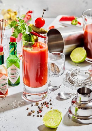 Photo for LONDON, UK - MARCH 15, 2023: Bloody mary cocktail with tabasco,strainer,shaker,lime and pepper on light background.Top view. - Royalty Free Image