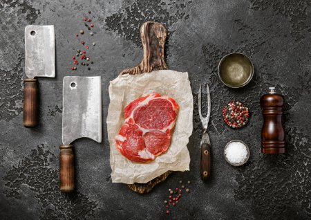 Photo for Red raw beef rib eye steak fillet with various meat utensils and gerbs on dark stone plate.Top view. - Royalty Free Image