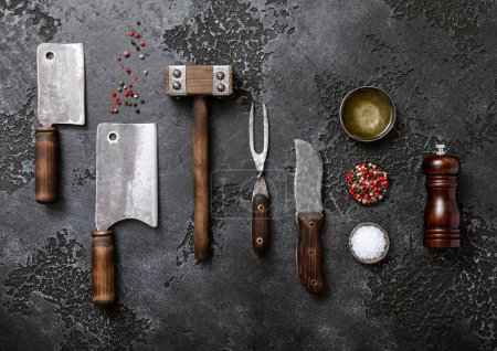 Photo for Kitchen meat utensils set on dark plate background. Meat cleaver,fork,knife with wooden tenderizer and various herbs and oil.Top view. - Royalty Free Image