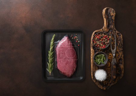 Photo for Chopping board with salt,pepper and rosemary with raw beef fillet sirloin steak in sealed tray on dark background.Top view. - Royalty Free Image