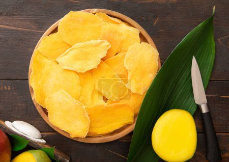 Téléchargez les photos : Assiette ronde avec morceaux de mangue séchés avec couteau et fruits crus. - en image libre de droit