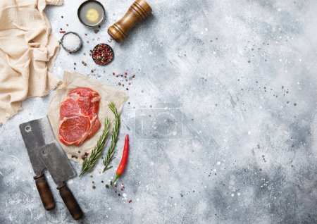 Photo for Raw beef rib eye steak on with meat cleaver on light kitchen table background with sal,pepper mill and oil. - Royalty Free Image