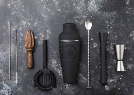 Photo for Black steel shaker,jigger,straw,manual juicer,muddler,wine opener on black stone with bar spoon and cocktail straw. - Royalty Free Image