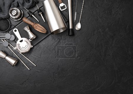 Foto de Coctelera de acero, colador, jigger y exprimidor de madera con barro en bandeja de goma negra con cuchara y paja plateada. - Imagen libre de derechos