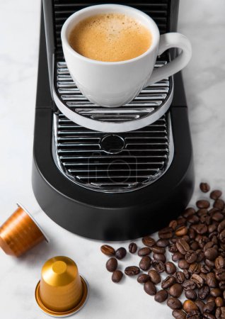Téléchargez les photos : Tasse à café blanche et machine à expresso maison avec capsules de café sur fond de cuisine en marbre blanc et haricots crus - en image libre de droit