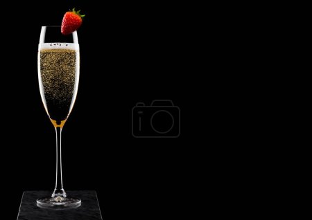 Téléchargez les photos : Élégant verre de champagne jaune avec fraise sur le dessus sur un panneau de marbre noir sur fond noir
. - en image libre de droit