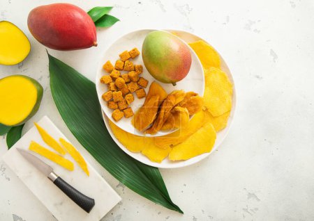 Photo for Dried sweet mango slices and balls on round plate with fruits and knife.Top view. - Royalty Free Image