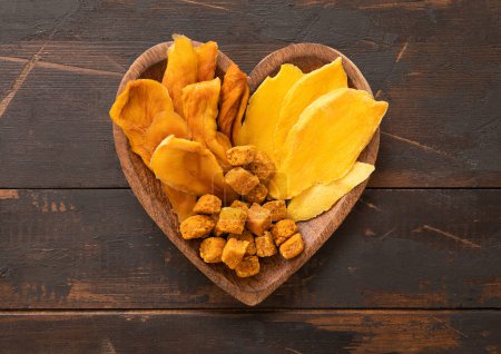 Téléchargez les photos : Assiette en bois en forme de coeur avec des tranches de mangue séchées et des boules.. - en image libre de droit