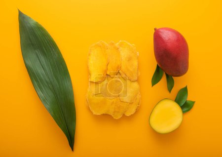 Photo for Sweet dried large mango slices on yellow background with raw fruit and leaf.Top view. - Royalty Free Image