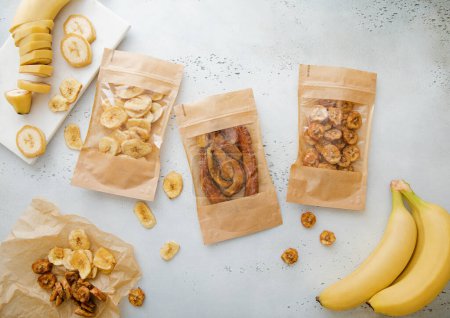 Photo for Packages of various crunchy and chewy banana slices with raw bananas on light board. - Royalty Free Image