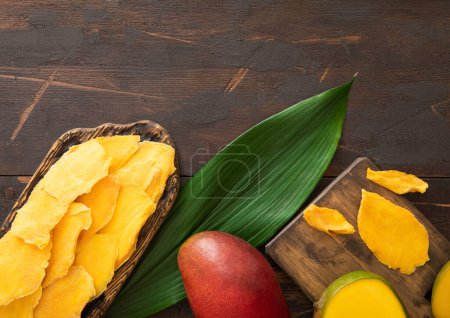 Téléchargez les photos : Planche à découper avec tranches de mangue séchées, feuille et couteau. - en image libre de droit
