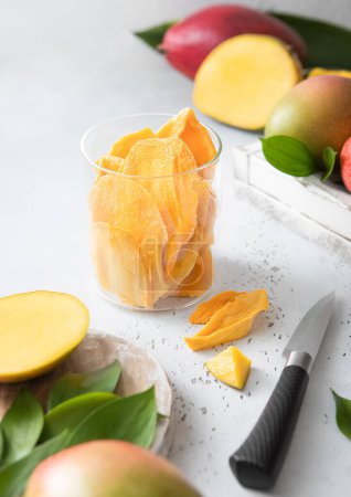 Téléchargez les photos : Mangue séchée dans un bocal en verre avec des fruits crus et un couteau sur un plateau léger.. - en image libre de droit