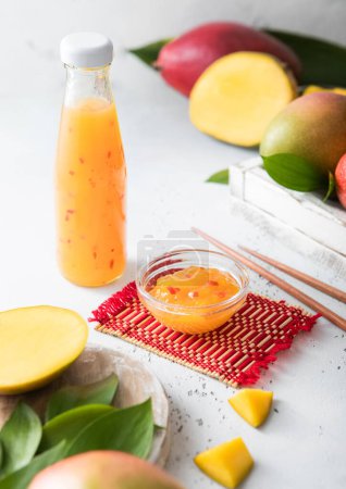 Téléchargez les photos : Sauce à la mangue en bouteille de verre sur fond clair avec des fruits frais. - en image libre de droit