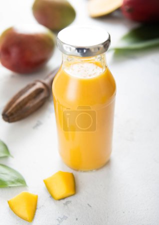 Foto de Botella de batido de mango fresco con piezas sobre fondo claro.. - Imagen libre de derechos