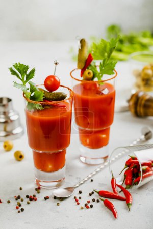 Foto de Vasos Bloody Mary con apio, aceitunas, pimiento rojo y cuchara de cóctel en el tablero de la barra de luz. - Imagen libre de derechos
