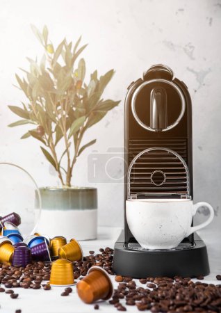 Photo for Coffee machine with cup and coffee capsules pods in light morning kitchen and sun light with coffee beans and plant - Royalty Free Image