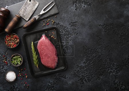 Photo for Raw beef fillet steak in vacuum tray with pepper on on black background with meat cleaver and fork.Top view. - Royalty Free Image
