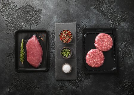 Photo for Raw fresh organic beef sirloin fillet steak and mince burgers sealed in vacuum tray with  on black background with spices.Top view. - Royalty Free Image