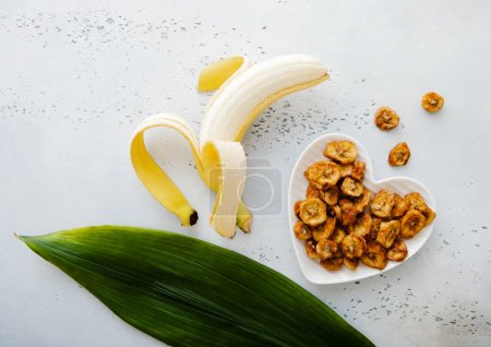 Foto de Rebanadas secas de plátano en forma de corazón con plátano crudo y hoja verde.Vista superior. - Imagen libre de derechos