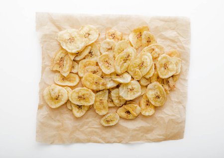 Photo for Dried crunchy banana chips on backing paper on white. - Royalty Free Image