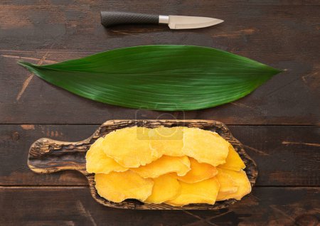 Téléchargez les photos : Planche à découper avec tranches de mangue séchées, feuilles et couteaux.. - en image libre de droit