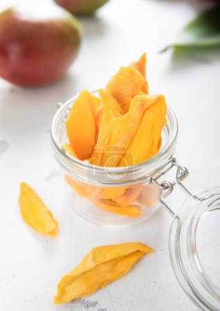 Téléchargez les photos : Tranches de mangue séchées sucrées avec des fruits crus frais sur fond clair.. - en image libre de droit