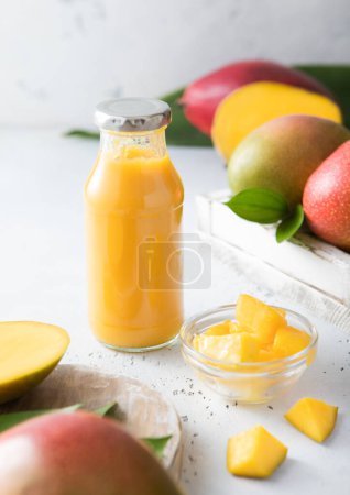 Téléchargez les photos : Smoothie à la mangue avec des morceaux crus en bouteille de verre sur la lumière avec des fruits frais. - en image libre de droit