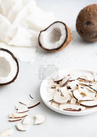 Foto de Placa con patatas fritas secas de coco orgánico y coco maduro entero sobre fondo claro. - Imagen libre de derechos