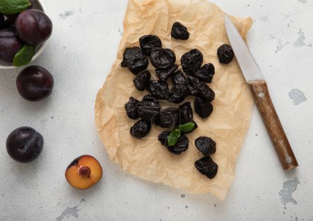 Téléchargez les photos : Pruneaux doux séchés aux prunes et couteau de cuisine sur fond clair. - en image libre de droit