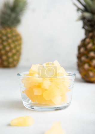 Photo for Dried soft sweet pineapple slices in glass bowl with raw pineapple on light table. - Royalty Free Image