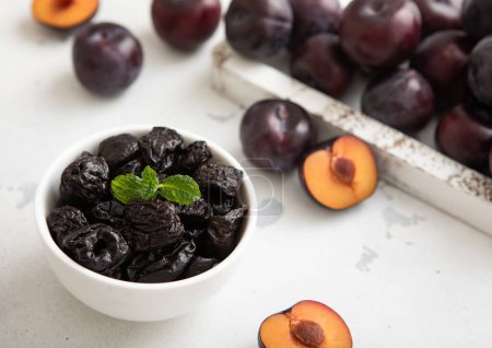 Téléchargez les photos : Pruneaux doux séchés avec prunes mûres dans une boîte en bois sur fond de cuisine léger.Macro - en image libre de droit