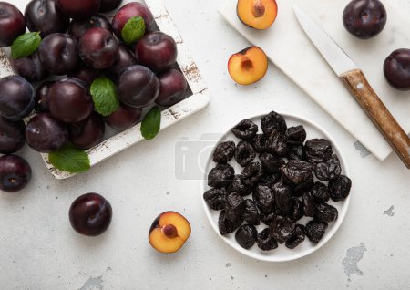 Téléchargez les photos : Assiette avec pruneaux sucrés séchés avec prunes mûres dans une boîte en bois sur fond de cuisine légère. - en image libre de droit