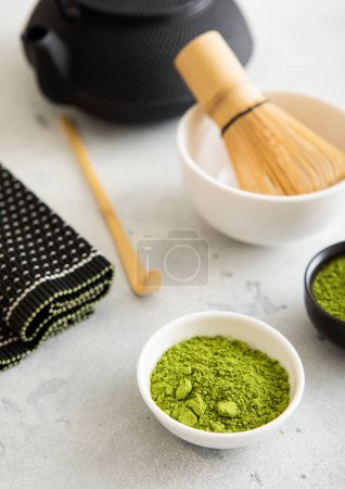 Photo for Matcha green tea powder with bamboo spoon and whisk in ceramic bowl with iron kettle on white. - Royalty Free Image