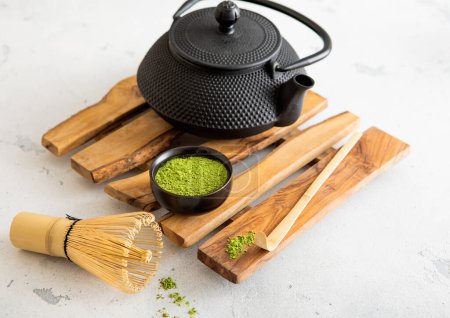 Foto de Polvo de té orgánico Matcha verde con hervidor de hierro fundido con batidor de bambú y cuchara en bandeja de madera. - Imagen libre de derechos