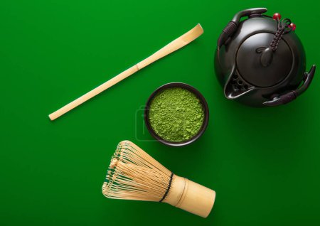 Photo for Organic matcha green tea powder set with bamboo whisk and spoon and ceramic kettle on green background. - Royalty Free Image