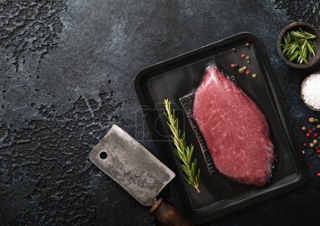 Photo for Fresh organic raw sirloin fillet steak with meat cleaver and rosemary,salt and pepper on dark kitchen background.Top view. - Royalty Free Image