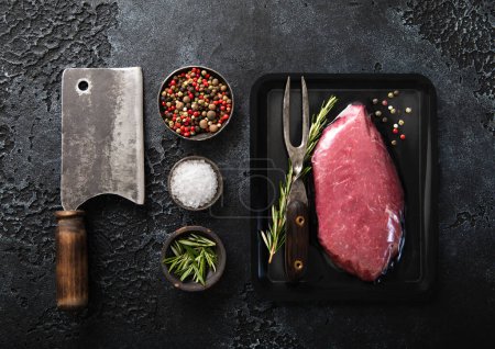 Photo for Fresh organic raw sirloin fillet steak with meat cleaver and rosemary,salt and pepper on black background.Top view. - Royalty Free Image