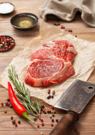 Photo for Rib eye steak fillet on with meat cleaver,salt and pepper on wooden table with tenderizer and kitchen towel. - Royalty Free Image