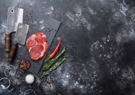 Photo for Raw Rib eye fillet on stone board with meat cleaver hatchets with salt and pepper with rosemary on black kitchen table.Top view. - Royalty Free Image